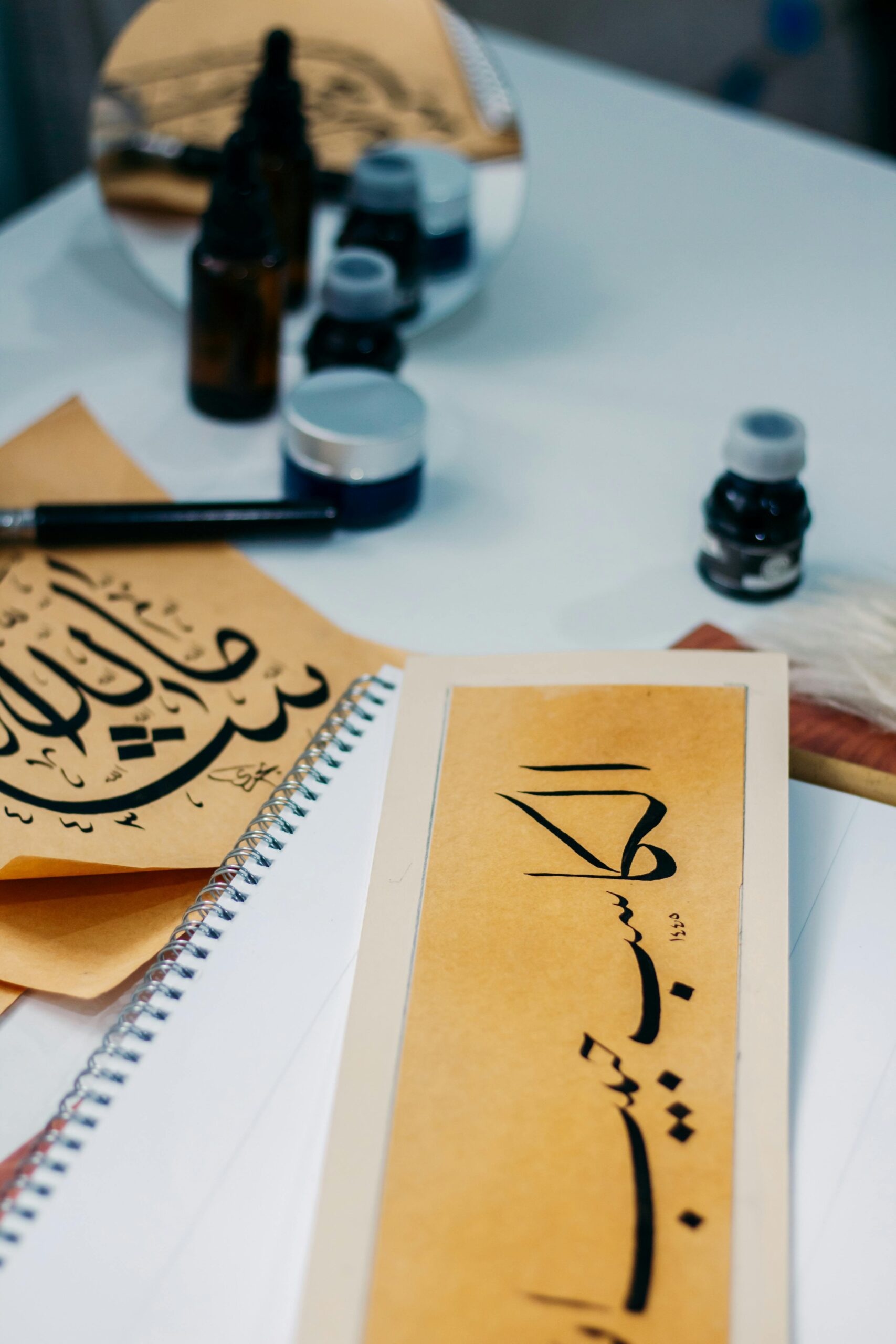 Accueil Close-up of Arabic calligraphy art with ink bottles and brush on a desk.